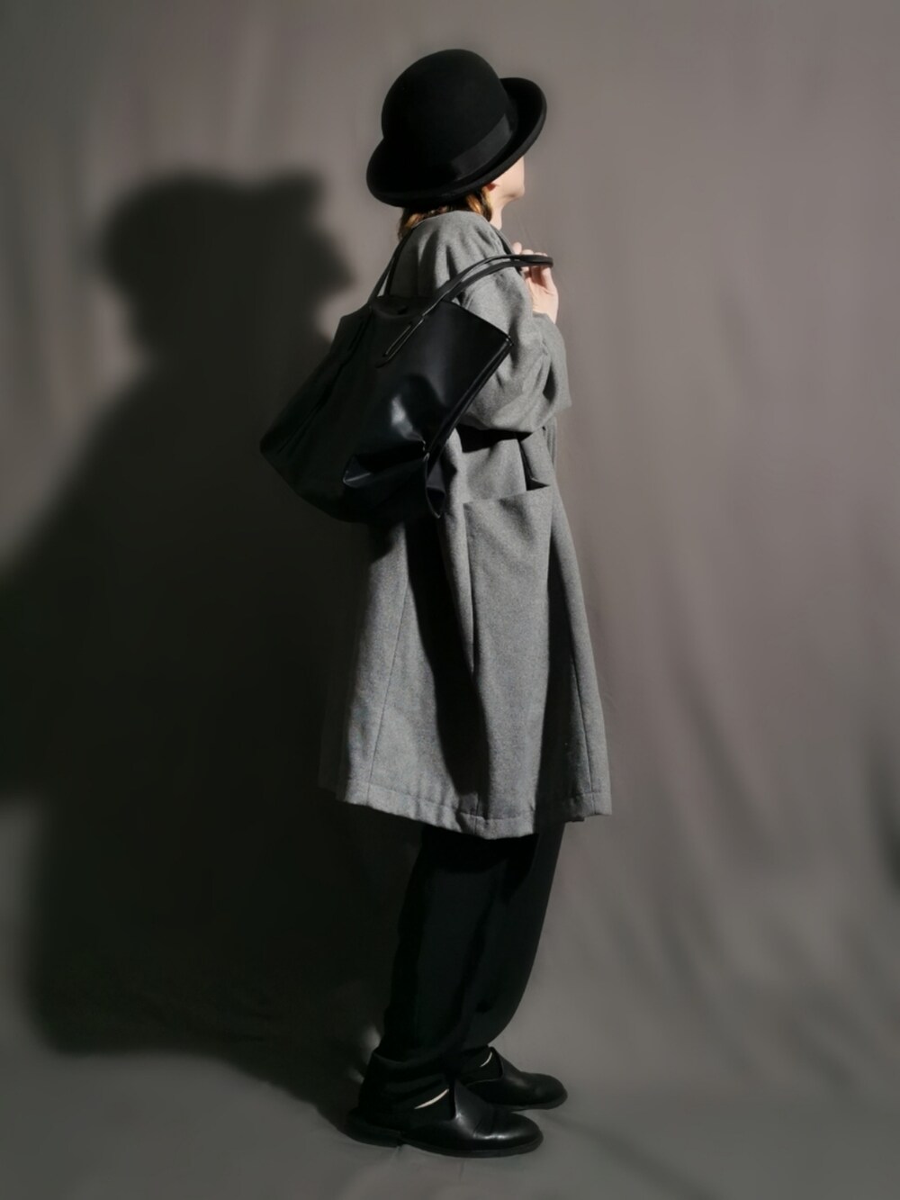 グレー系のチェスターコート、ブラック系のトートバッグ、ブラック系のパンツを着用したメンズの冬コーディネートの3枚目の写真