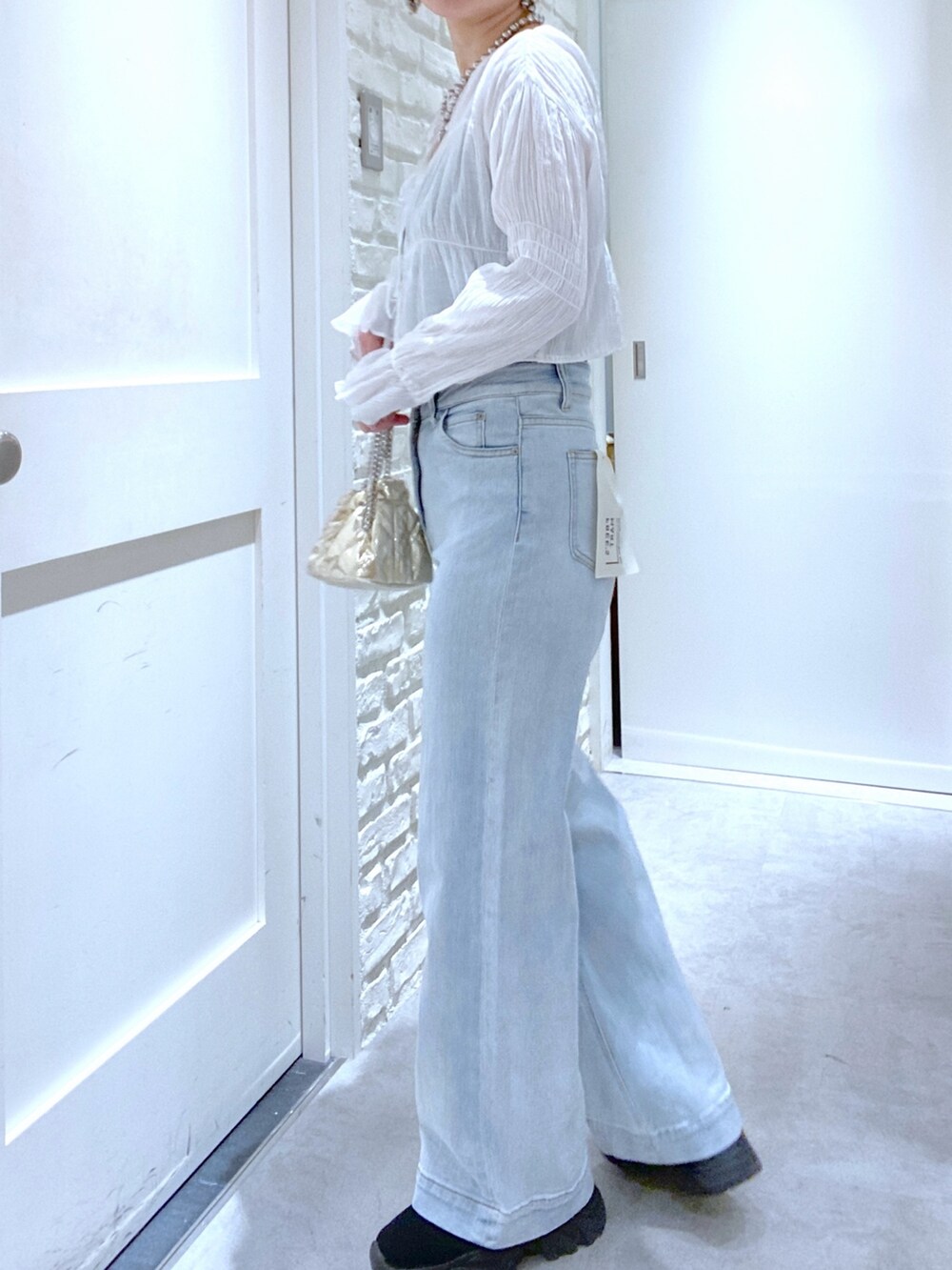 ブラック系のブーツ、ホワイト系のシャツ/ブラウス、ゴールド系のショルダーバッグを着用したレディースの春コーディネートの2枚目の写真