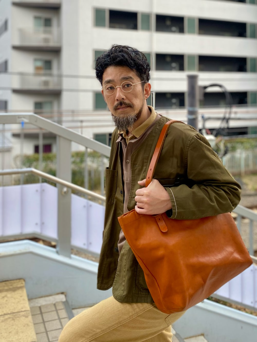 ゴールド系のデニムパンツ、ブラウン系のブーツ、オレンジ系のトートバッグを着用したメンズの春コーディネートの2枚目の写真