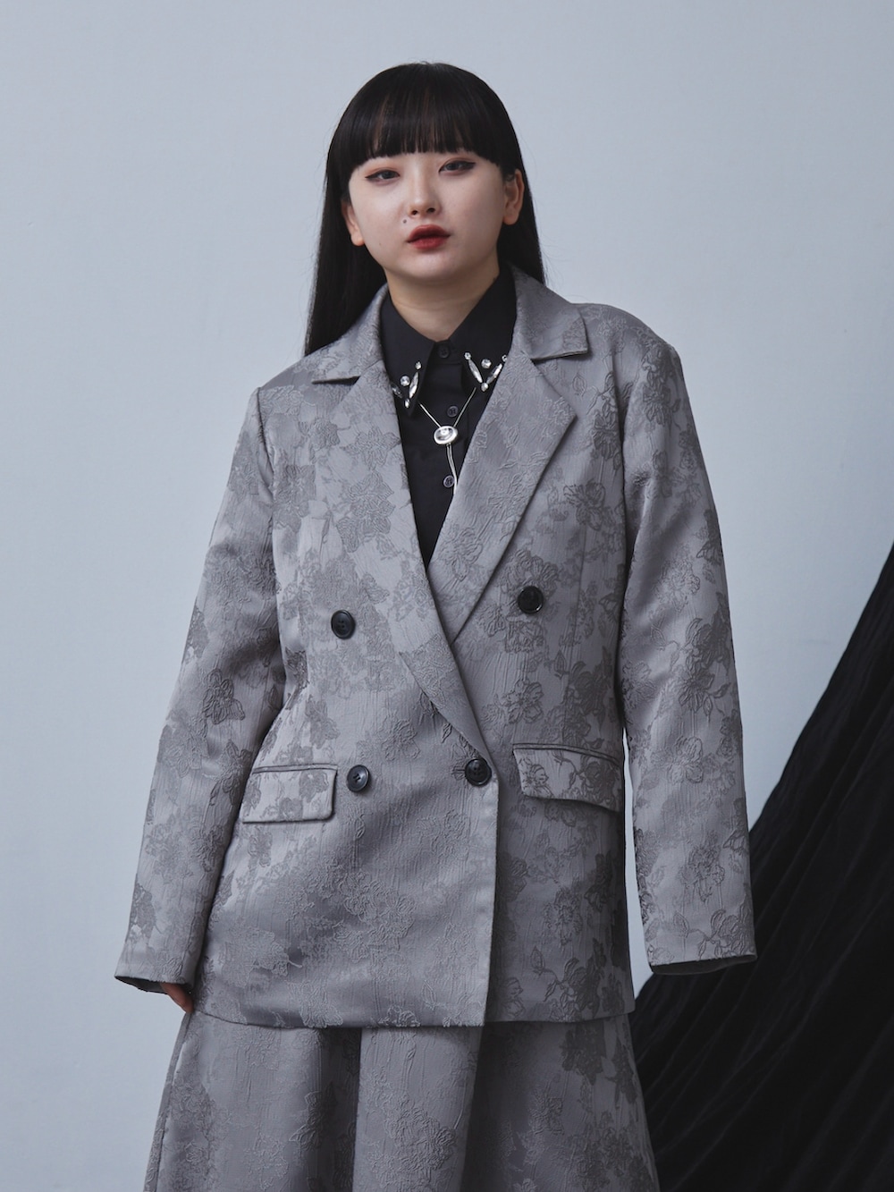 グレー系のテーラードジャケット、グレー系のスカート、ブラック系のシャツ/ブラウスを着用したレディースの秋コーディネートの2枚目の写真