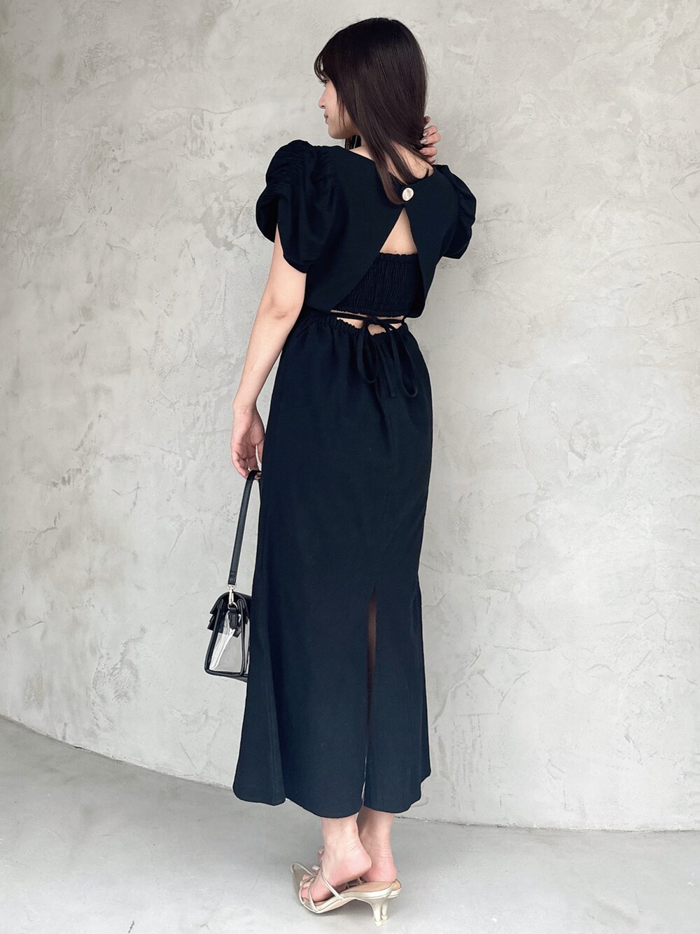 ブラック系のワンピース、ブラック系のハンドバッグ、ゴールド系のサンダルを着用したレディースの春コーディネートの2枚目の写真