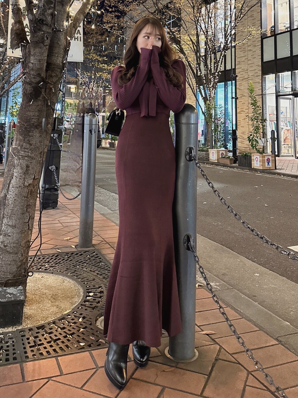 レッド系のワンピース、ブラック系のショルダーバッグ、ブラック系のブーツを着用したレディースの秋コーディネートの2枚目の写真