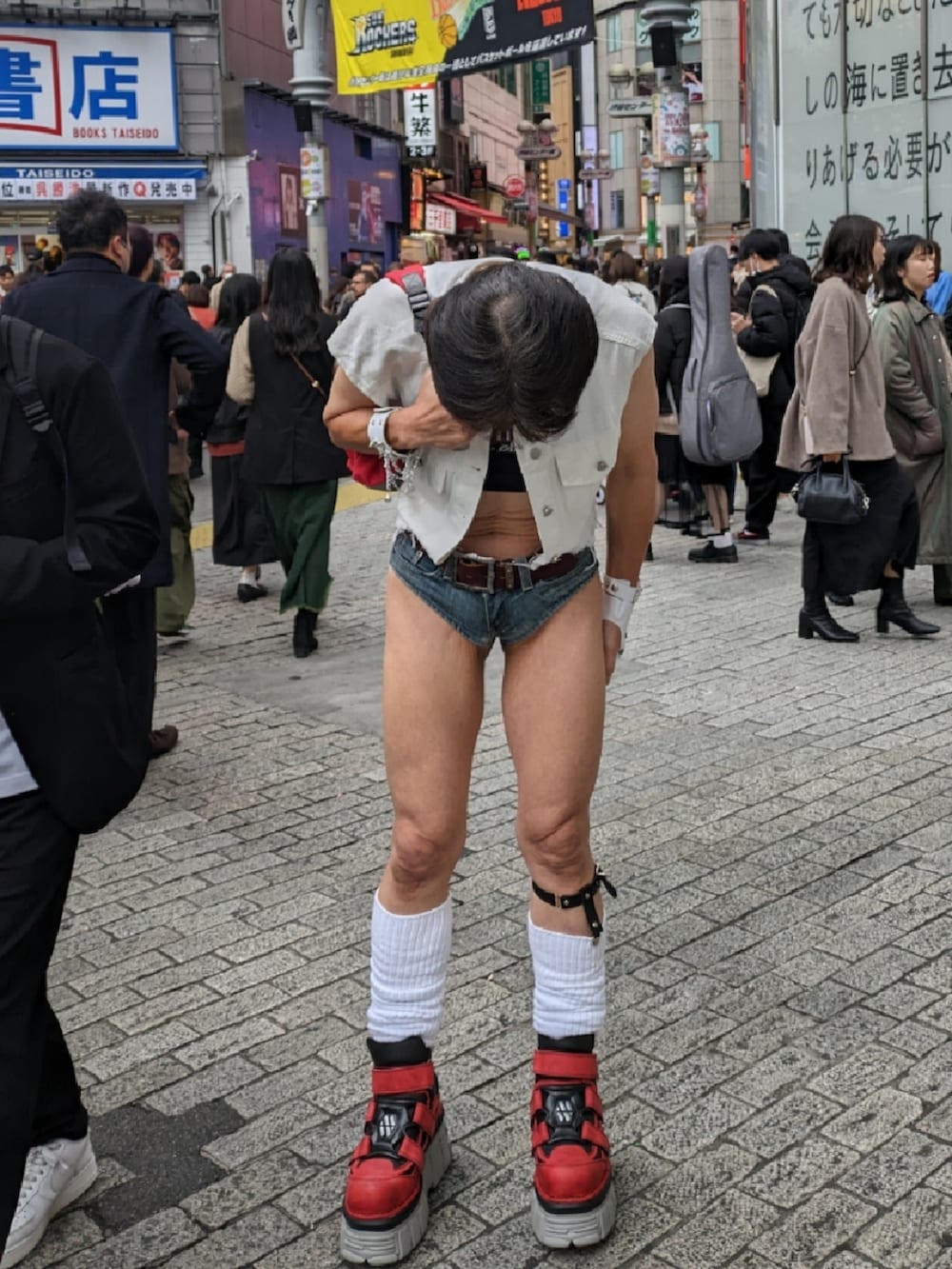 レッド系のスニーカー、ブルー系のデニムパンツ、ホワイト系のベストを着用したメンズの秋コーディネートの3枚目の写真