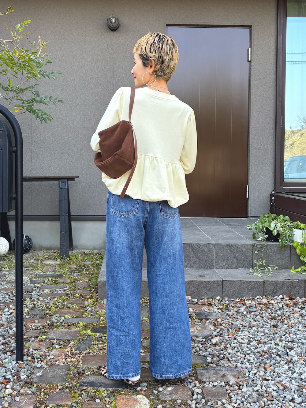 イエロー系のニット/セーター、ブラウン系のショルダーバッグ、ブルー系のデニムパンツを着用したレディースの冬コーディネートの3枚目の写真