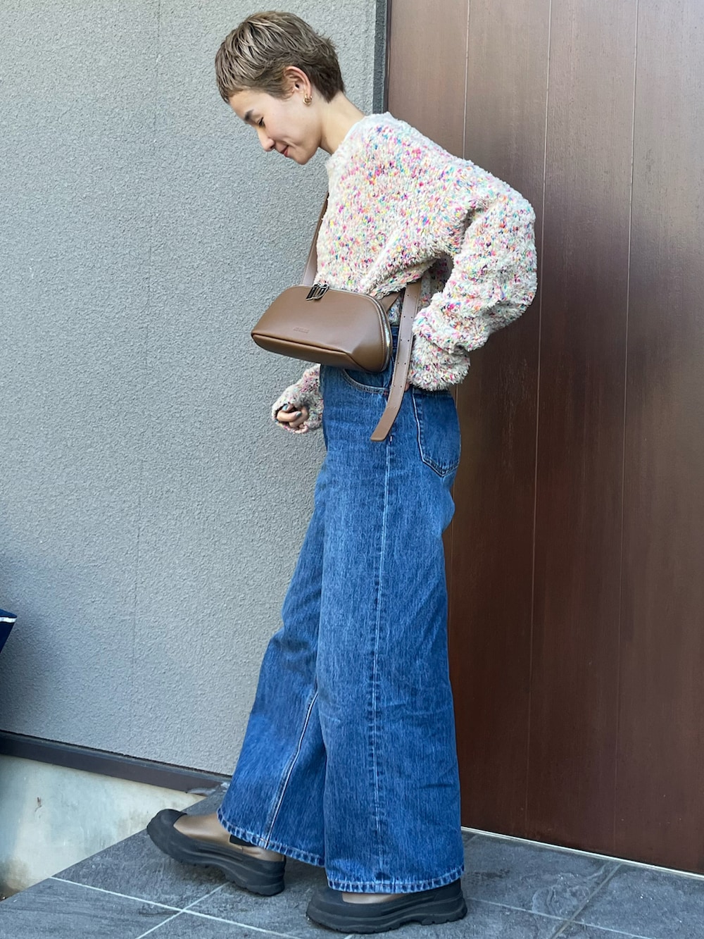 ブラウン系のショルダーバッグ、ベージュ系のニット/セーター、ブルー系のデニムパンツを着用したレディースの秋コーディネートの2枚目の写真