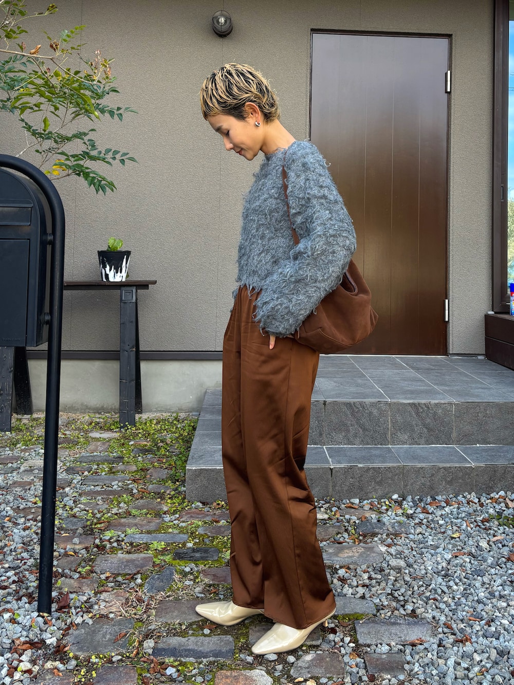 グレー系のニット/セーター、ブラウン系のショルダーバッグ、ブラウン系のスラックスを着用したレディースの冬コーディネートの2枚目の写真