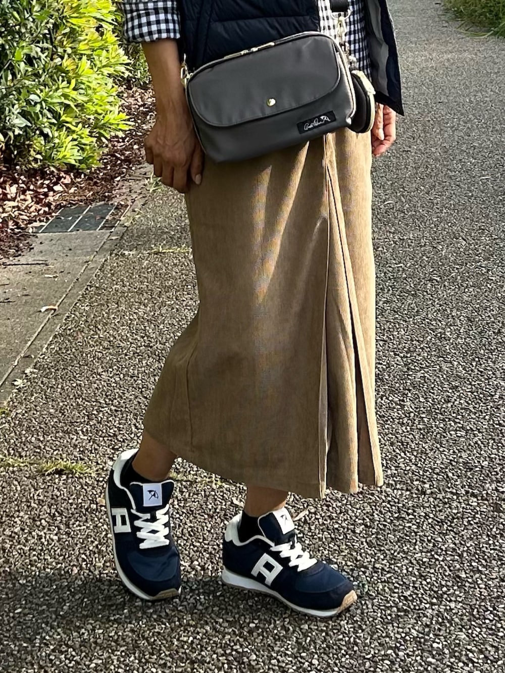 グレー系のショルダーバッグ、グリーン系のダウンベスト、ブルー系のスニーカーを着用したレディースの秋コーディネートの2枚目の写真