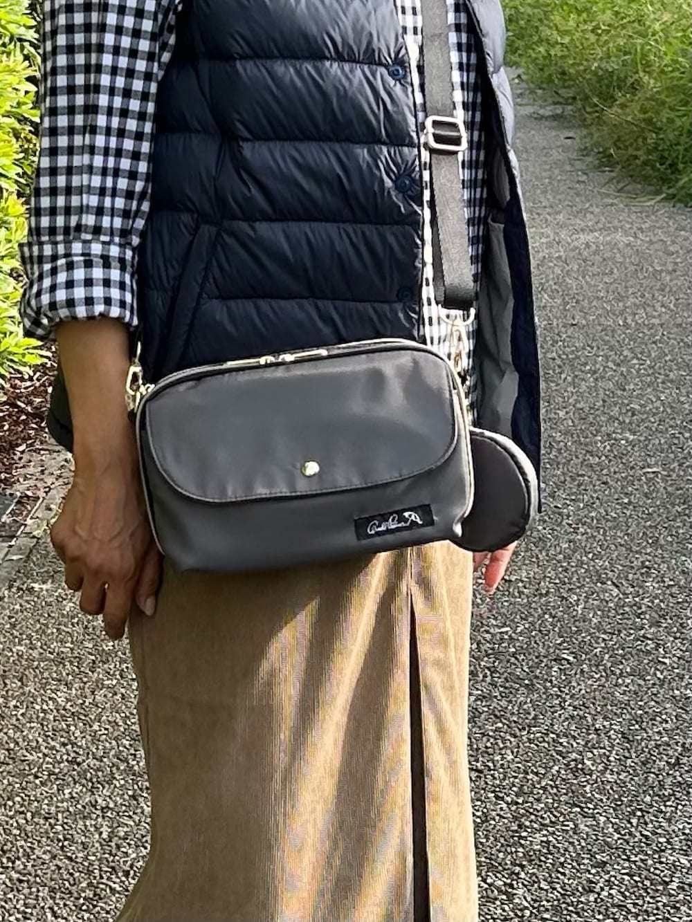 グレー系のショルダーバッグ、グリーン系のダウンベスト、ブルー系のスニーカーを着用したレディースの秋コーディネートの3枚目の写真