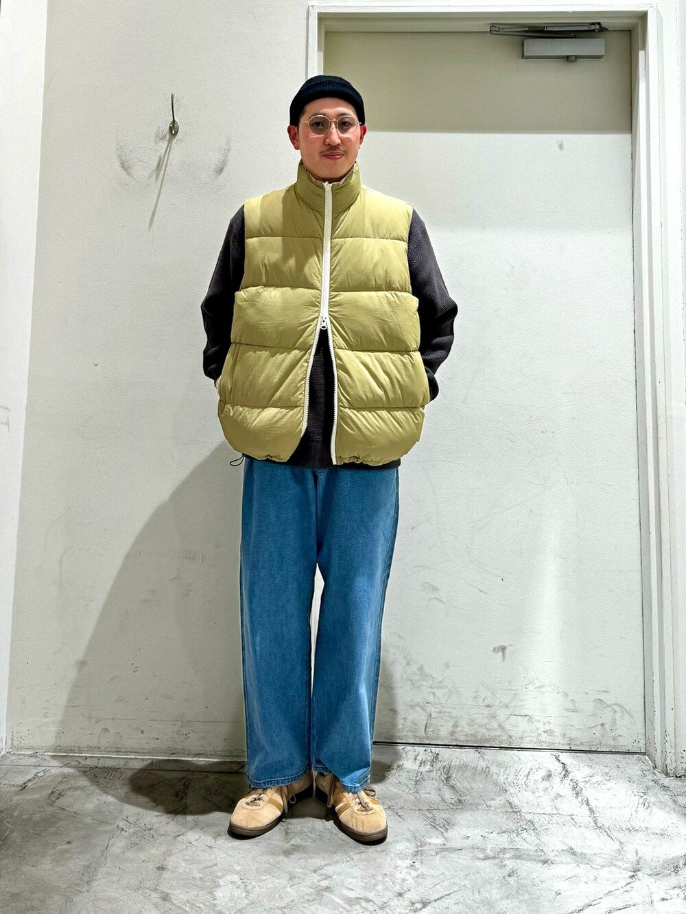 ホワイト系のダウンベスト、グレー系のニット/セーター、ブルー系のデニムパンツを着用したメンズの秋コーディネートの2枚目の写真