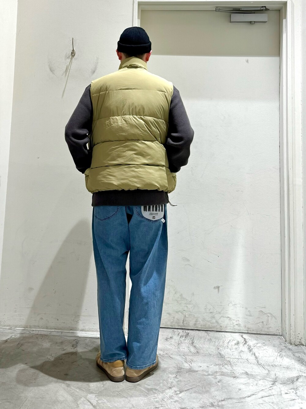 ホワイト系のダウンベスト、グレー系のニット/セーター、ブルー系のデニムパンツを着用したメンズの秋コーディネートの4枚目の写真