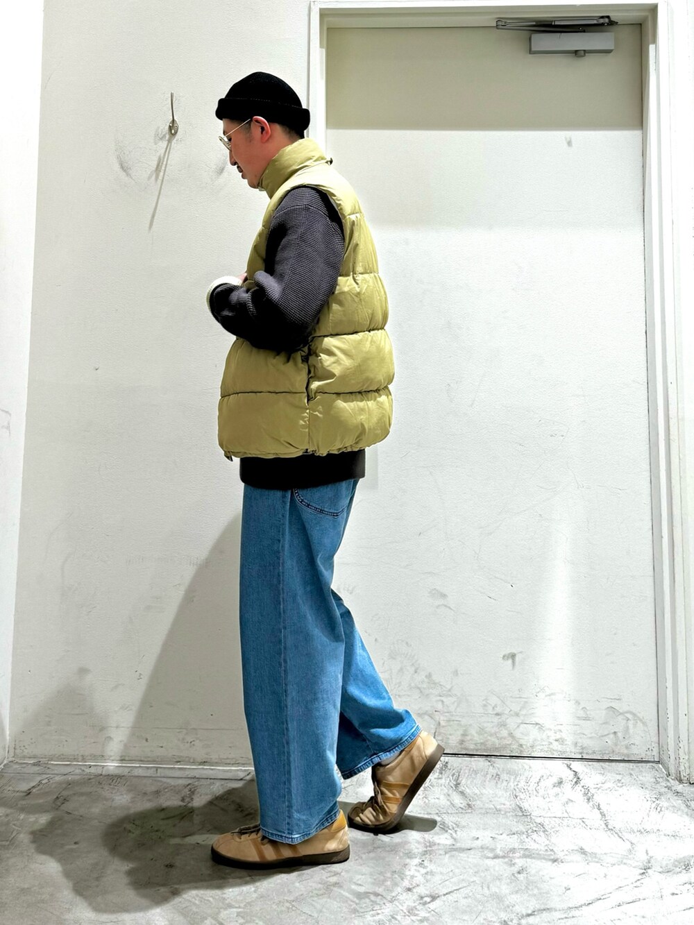 ホワイト系のダウンベスト、グレー系のニット/セーター、ブルー系のデニムパンツを着用したメンズの秋コーディネートの3枚目の写真