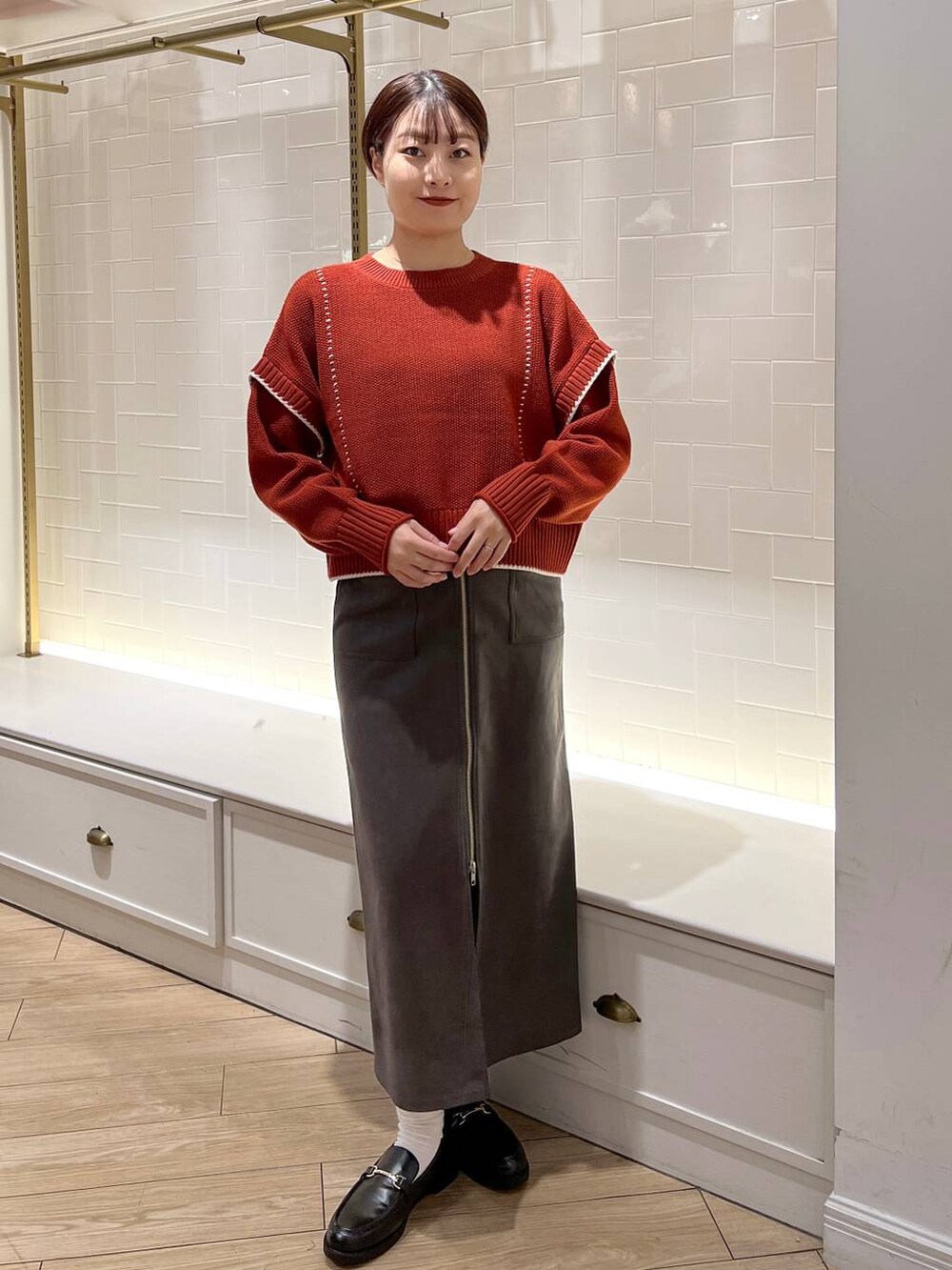 レッド系のニット/セーター、グレー系のスカート、ブラック系のローファーを着用したレディースの秋コーディネートの2枚目の写真