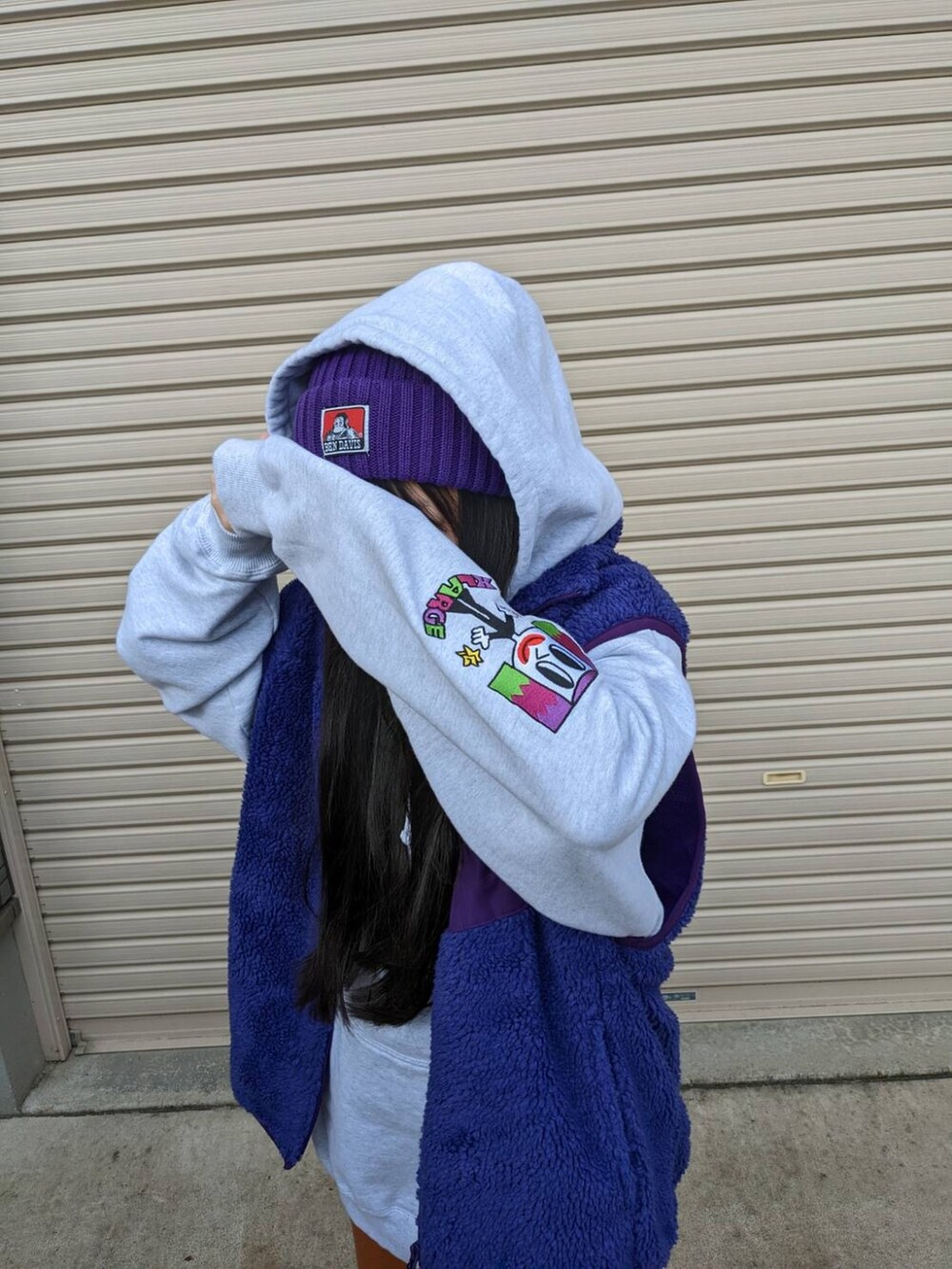 パープル系のベスト、グレー系のパーカー、ホワイト系のスニーカーを着用したレディースの冬コーディネートの3枚目の写真