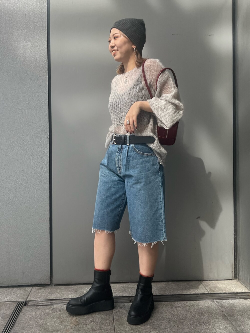 ブルー系のデニムパンツ、グレー系のニット/セーター、レッド系のハンドバッグを着用したレディースの秋コーディネートの2枚目の写真