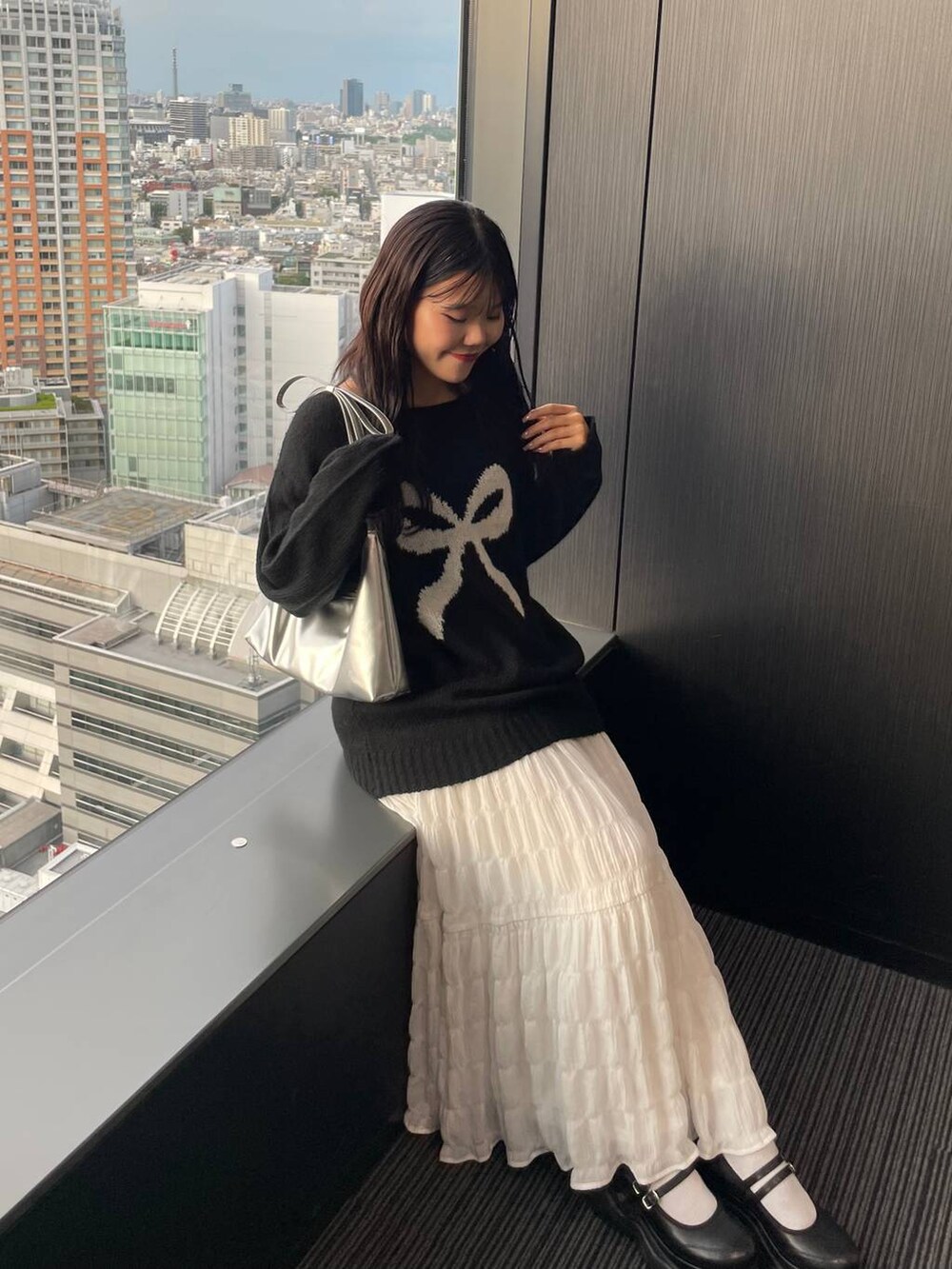 シルバー系のショルダーバッグ、ホワイト系のスカート、ブラック系のニット/セーターを着用したレディースの秋コーディネートの2枚目の写真