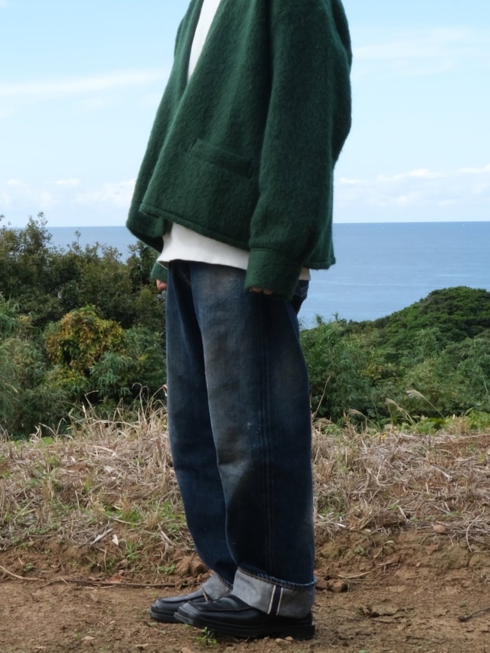 グリーン系のカーディガン/ボレロ、ブラック系のローファー、ブルー系のデニムパンツを着用したメンズの秋コーディネートの3枚目の写真