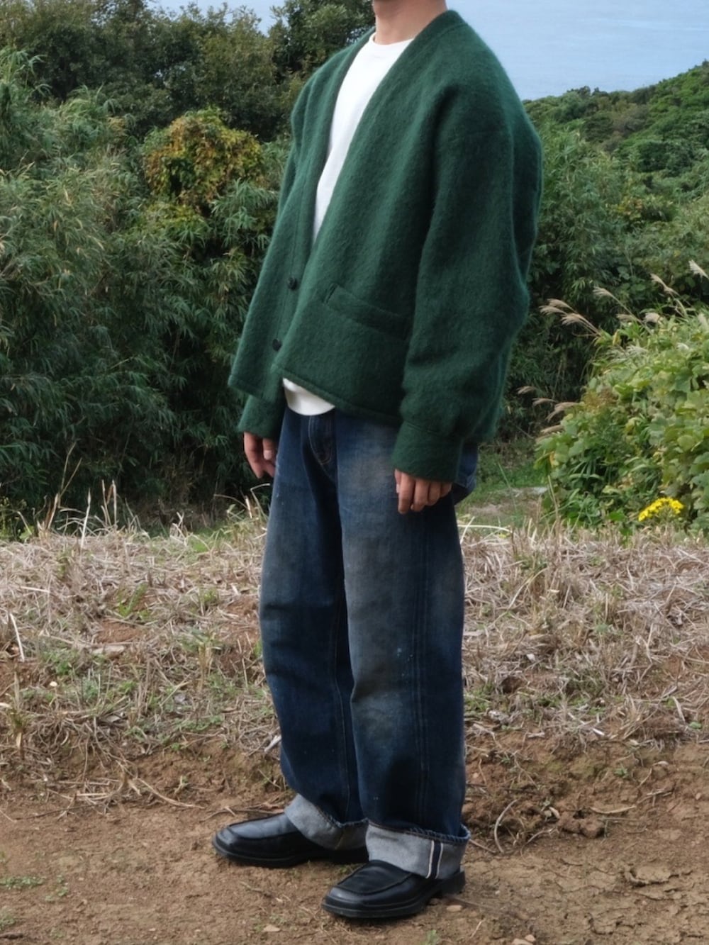 グリーン系のカーディガン/ボレロ、ブラック系のローファー、ブルー系のデニムパンツを着用したメンズの秋コーディネートの2枚目の写真