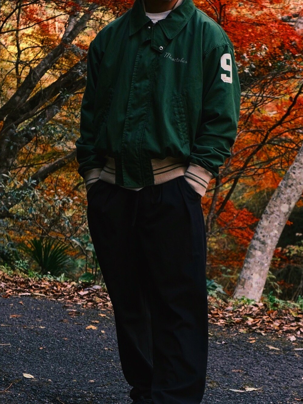 グリーン系のスタジャン、ブラック系のスラックス、ブラック系のスニーカーを着用したメンズの秋コーディネートの2枚目の写真
