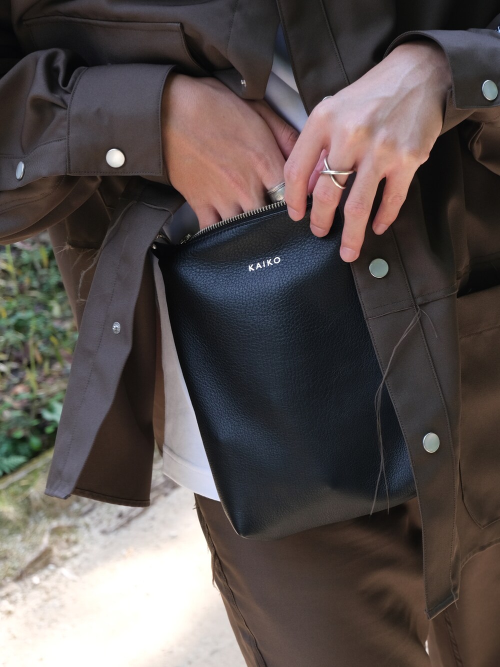 ブラウン系のセットアップ、ホワイト系のスニーカー、ブラック系のショルダーバッグを着用したメンズの秋コーディネートの2枚目の写真