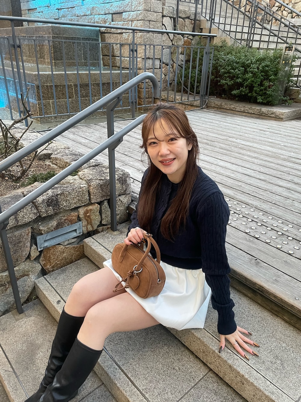 ブルー系のカーディガン/ボレロ、ホワイト系のスカート、ベージュ系のボストンバッグを着用したレディースの春コーディネートの3枚目の写真