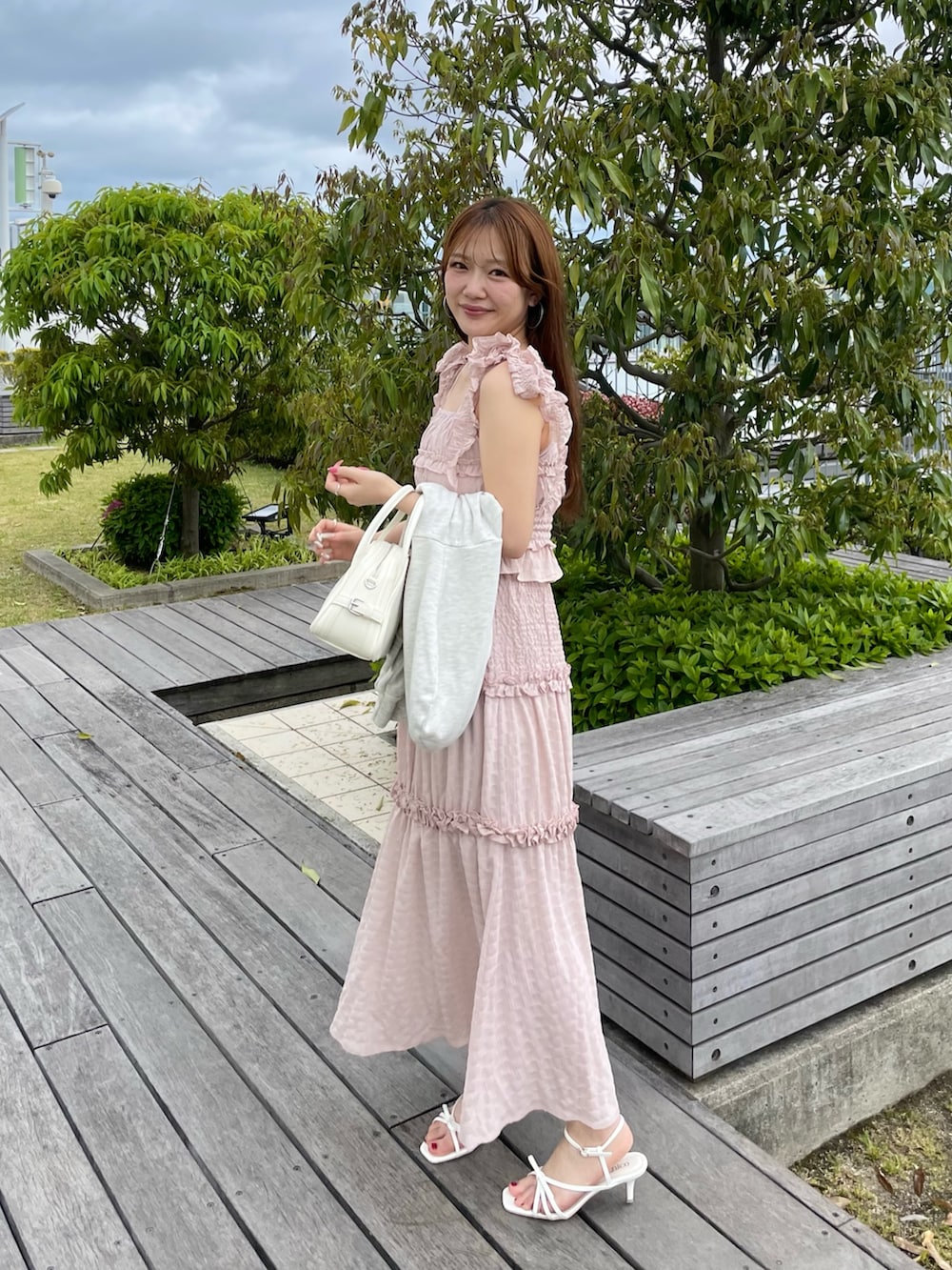 ピンク系のワンピース、ベージュ系のパーカー、ホワイト系のボストンバッグを着用したレディースの春コーディネートの2枚目の写真