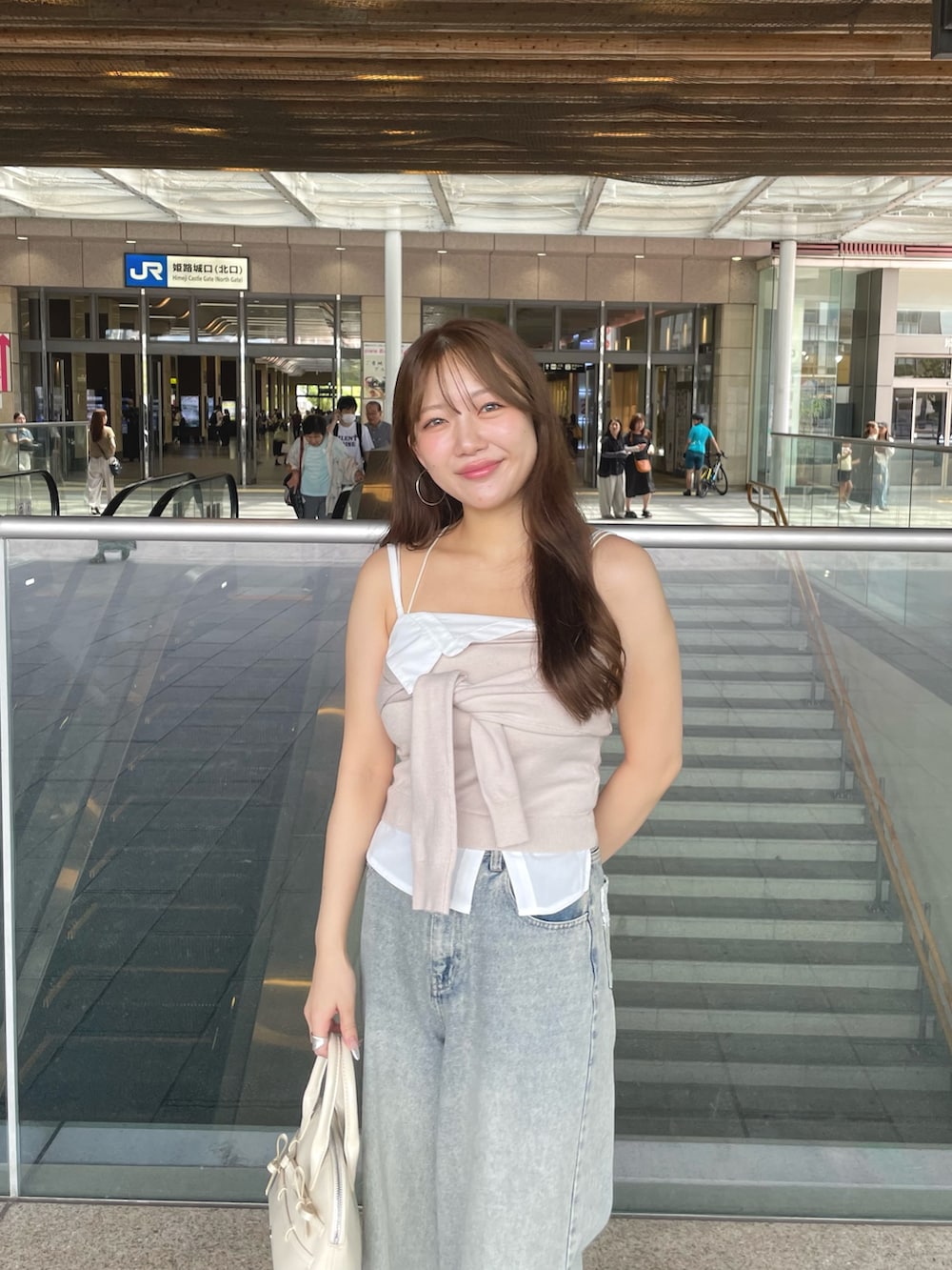 ベージュ系のキャミソール、ブルー系のデニムパンツ、ホワイト系のボストンバッグを着用したレディースの夏コーディネートの2枚目の写真