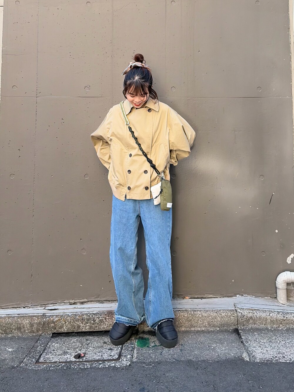 ベージュ系のトレンチコート、ブルー系のデニムパンツ、グレー系のシュシュを着用したレディースの冬コーディネートの2枚目の写真