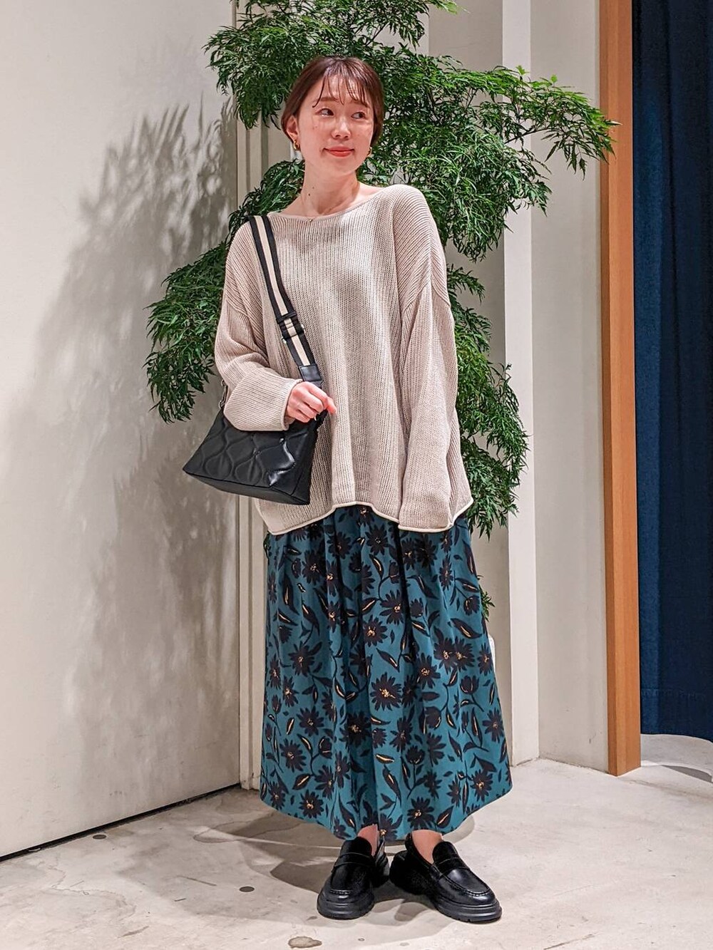 ブラック系のショルダーバッグ、ベージュ系のニット/セーター、グリーン系のスカートを着用したレディースの春コーディネートの2枚目の写真