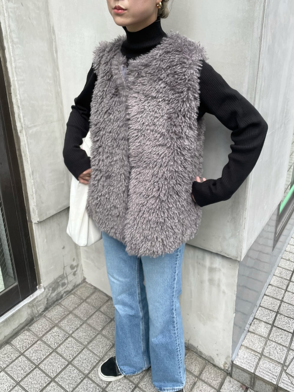 グレー系のベスト、ブラック系のニット/セーター、ブルー系のデニムパンツを着用したレディースの秋コーディネートの3枚目の写真