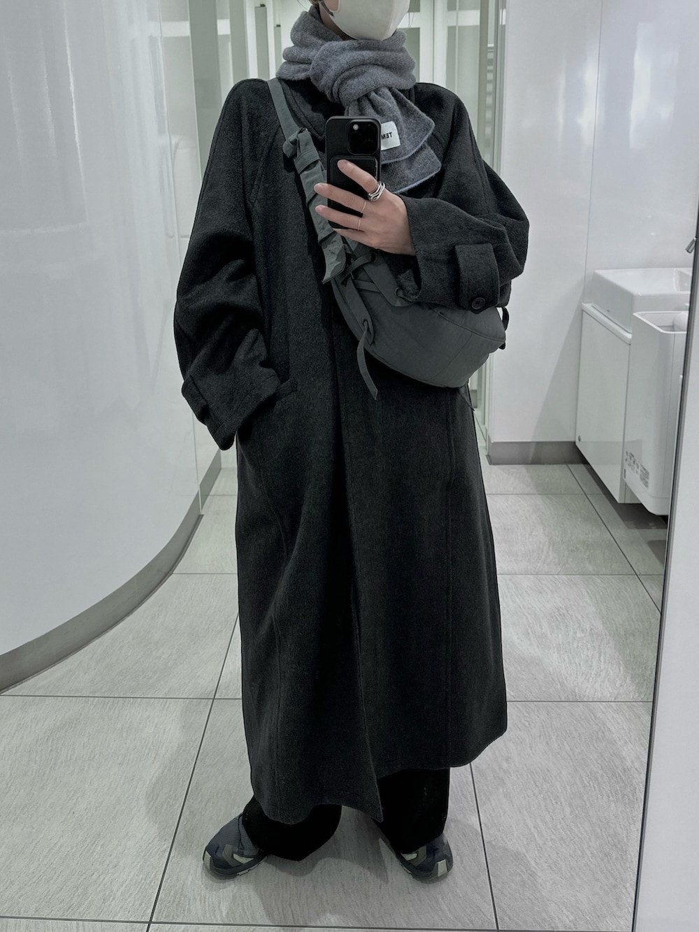 グレー系のステンカラーコート、グリーン系のスニーカー、ブラック系のショルダーバッグを着用したレディースの冬コーディネートの3枚目の写真