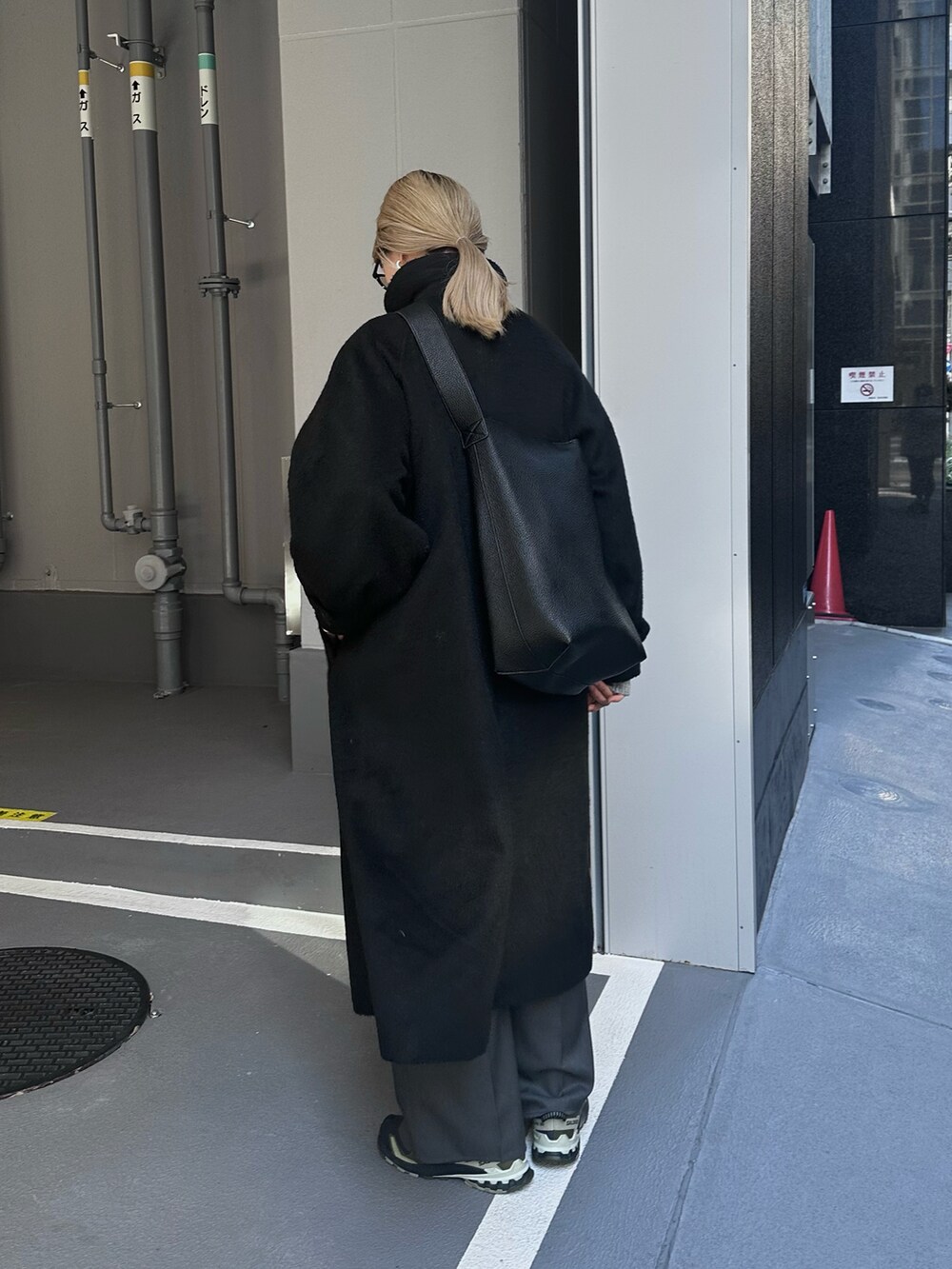 ブラック系のステンカラーコート、グレー系のスラックス、ブラック系のショルダーバッグを着用したレディースの冬コーディネートの3枚目の写真