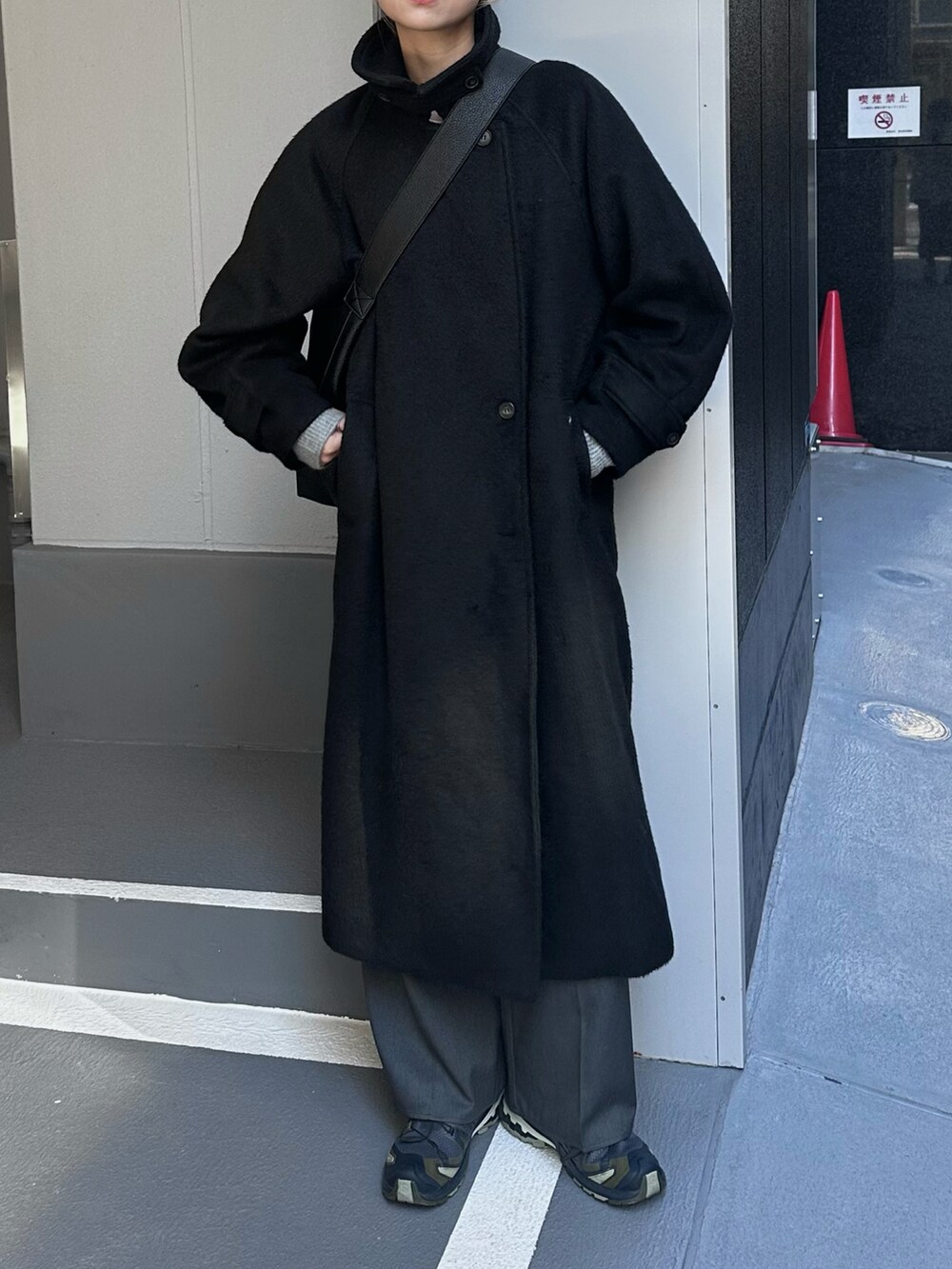 ブラック系のステンカラーコート、グレー系のスラックス、ブラック系のショルダーバッグを着用したレディースの冬コーディネートの2枚目の写真