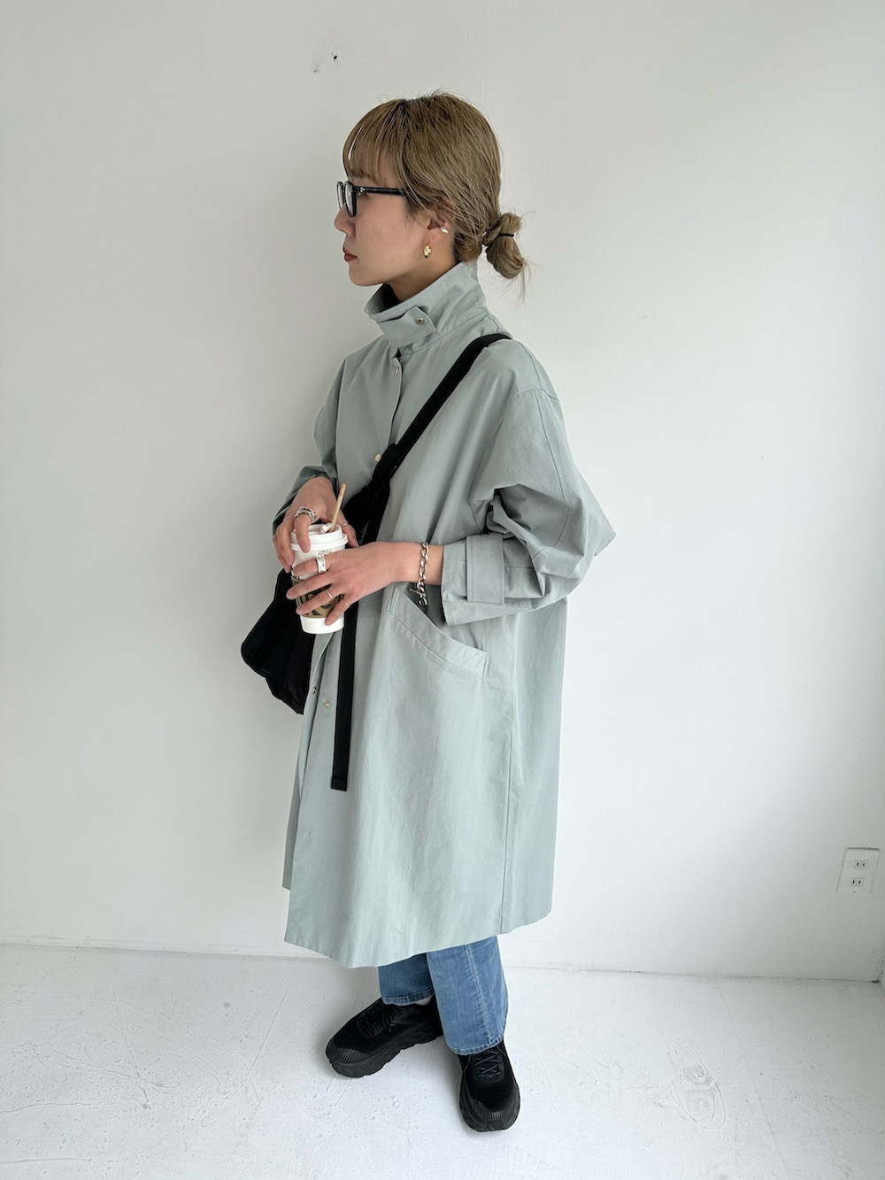 ブルー系のステンカラーコート、ブルー系のデニムパンツ、ブラック系のショルダーバッグを着用したレディースの冬コーディネートの4枚目の写真