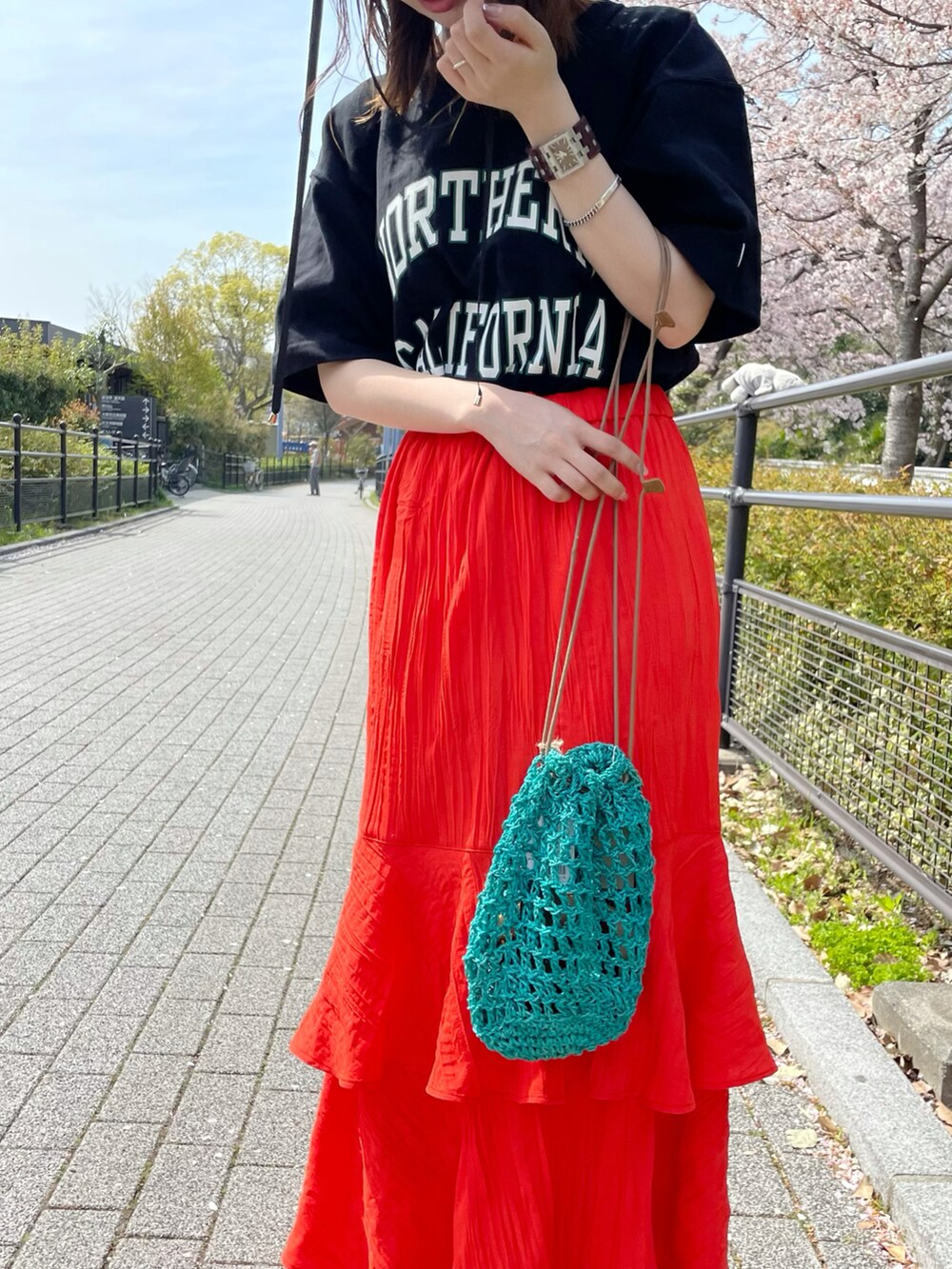 グリーン系のショルダーバッグ、オレンジ系のスカート、ブラック系のTシャツ/カットソーを着用したレディースの春コーディネートの2枚目の写真