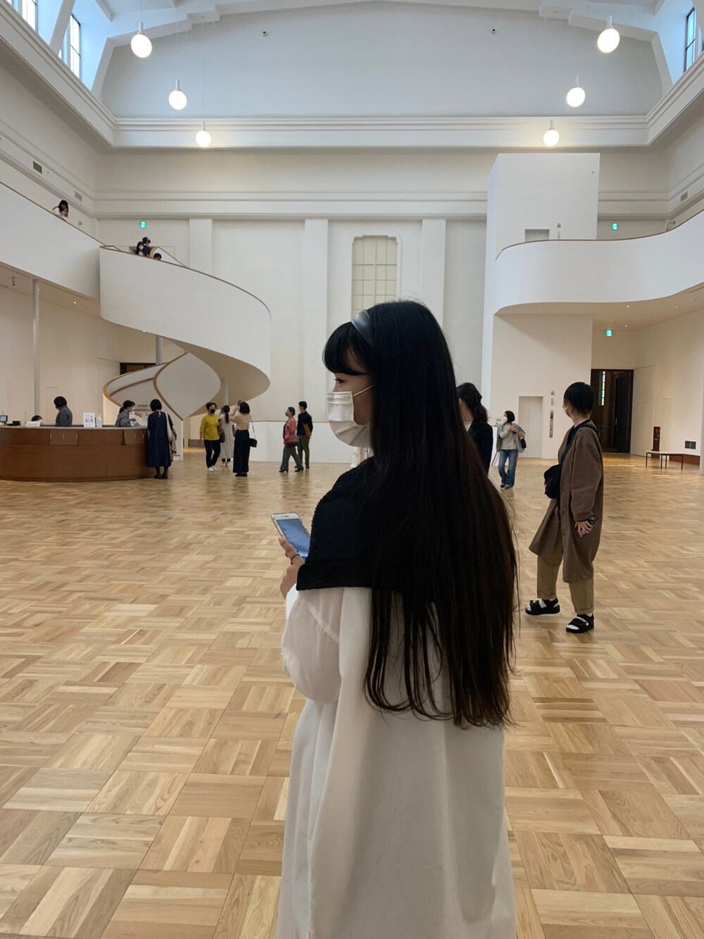 ブラック系のショルダーバッグ、ホワイト系のシャツワンピース、ブラック系のピアス（両耳用）を着用したレディースの春コーディネートの2枚目の写真