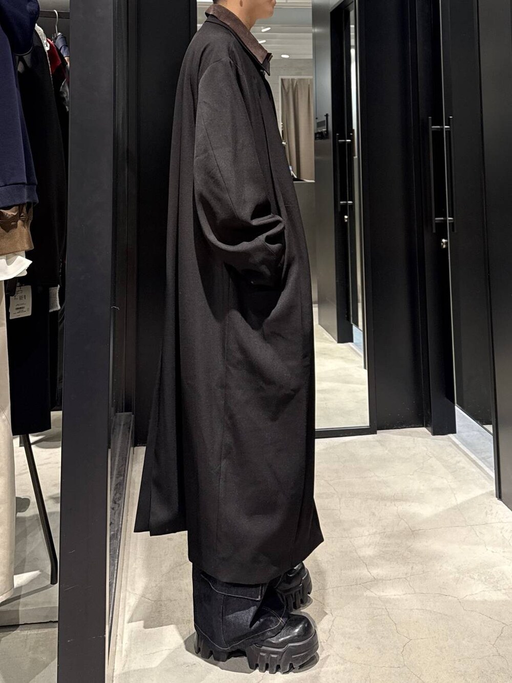 ブラック系のステンカラーコート、ブルー系のデニムパンツ、ホワイト系のネックレスを着用したメンズの冬コーディネートの2枚目の写真