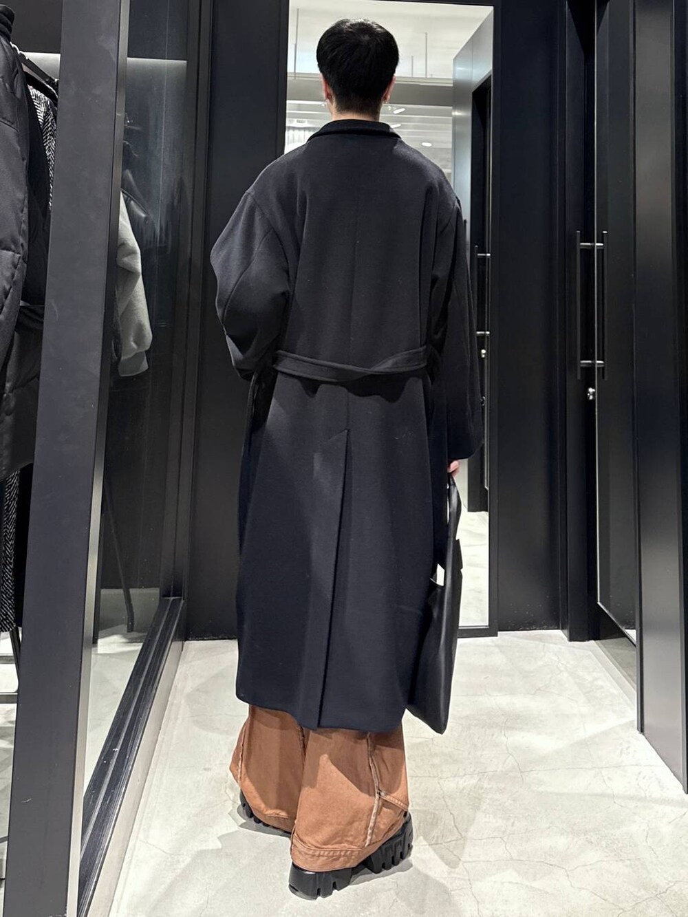 ブラック系のトートバッグ、ブラック系のカーディガン/ボレロ、オレンジ系のデニムパンツを着用したメンズの冬コーディネートの2枚目の写真