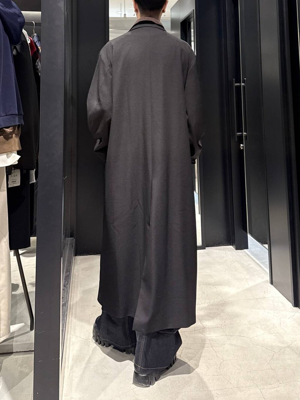 ブラック系のステンカラーコート、ブルー系のデニムパンツ、ホワイト系のネックレスを着用したメンズの冬コーディネートの3枚目の写真