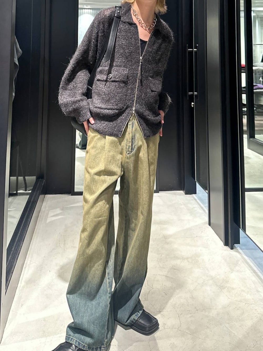 グリーン系のデニムパンツ、ブラック系のニット/セーター、ブラック系のショルダーバッグを着用したメンズの秋コーディネートの2枚目の写真