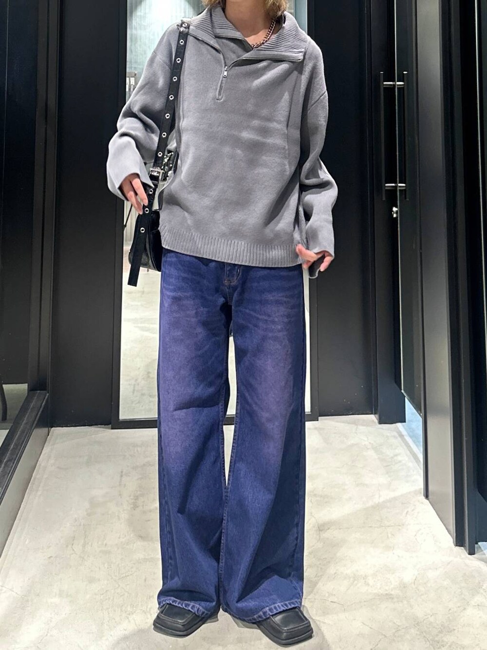 パープル系のデニムパンツ、グレー系のニット/セーター、ブラック系のショルダーバッグを着用したメンズの秋コーディネートの3枚目の写真