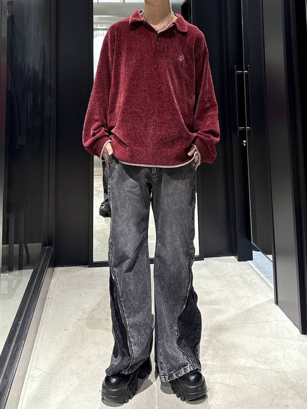 レッド系のニット/セーター、ブラック系のデニムパンツ、シルバー系のネックレスを着用したメンズの冬コーディネートの3枚目の写真