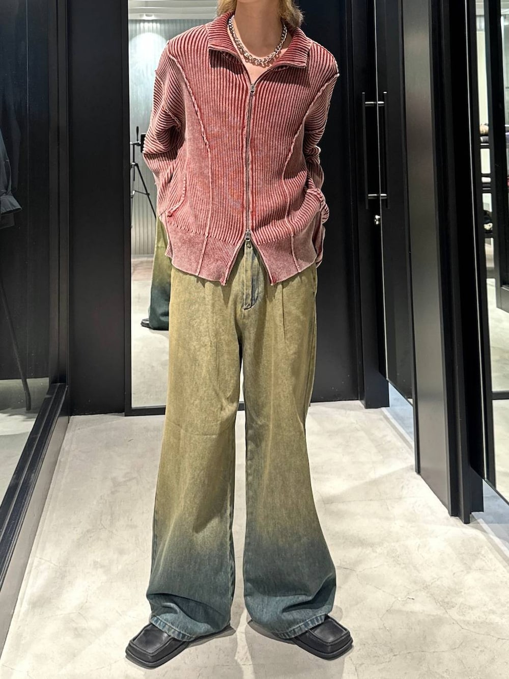 グリーン系のデニムパンツ、オレンジ系のニット/セーター、シルバー系のネックレスを着用したメンズの秋コーディネートの2枚目の写真