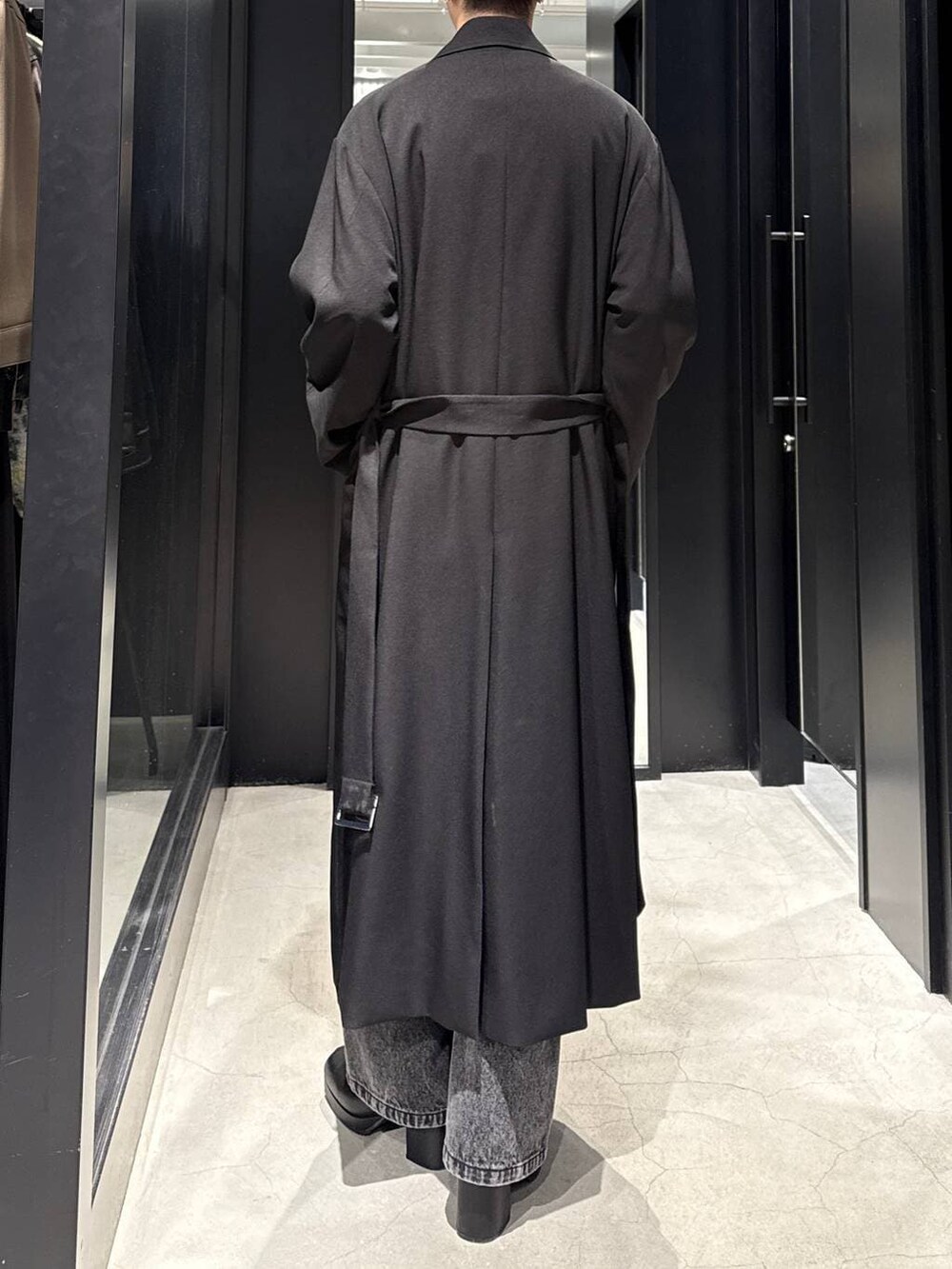 ブラック系のブーツ、ブラック系のステンカラーコート、ブラック系のデニムパンツを着用したメンズの冬コーディネートの4枚目の写真