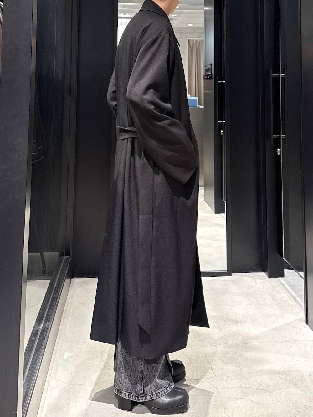 ブラック系のブーツ、ブラック系のステンカラーコート、ブラック系のデニムパンツを着用したメンズの冬コーディネートの2枚目の写真