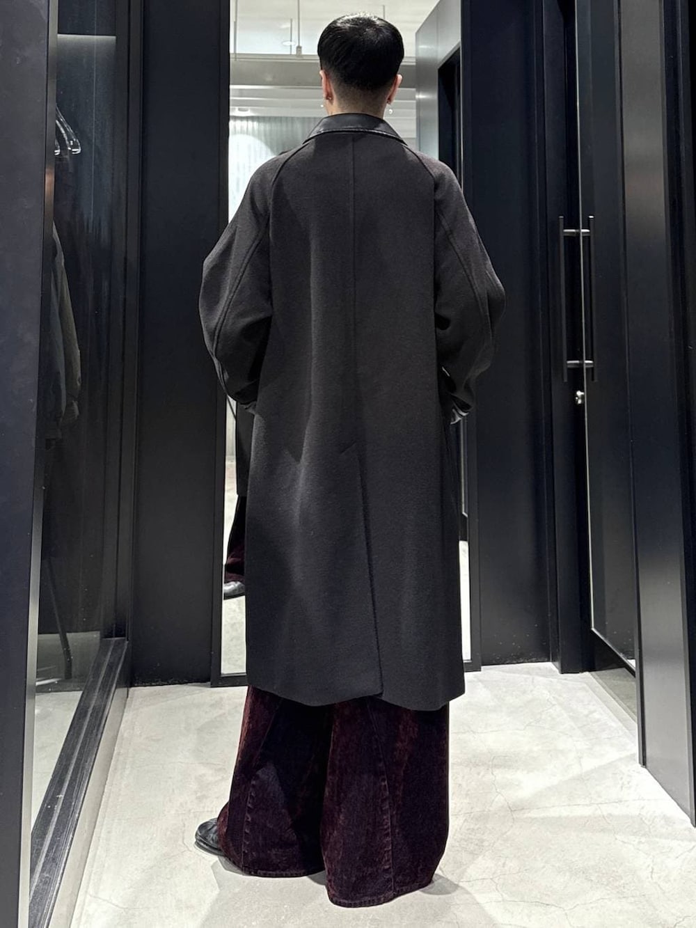 ブラック系のステンカラーコート、レッド系のデニムパンツを着用したメンズの秋コーディネートの3枚目の写真