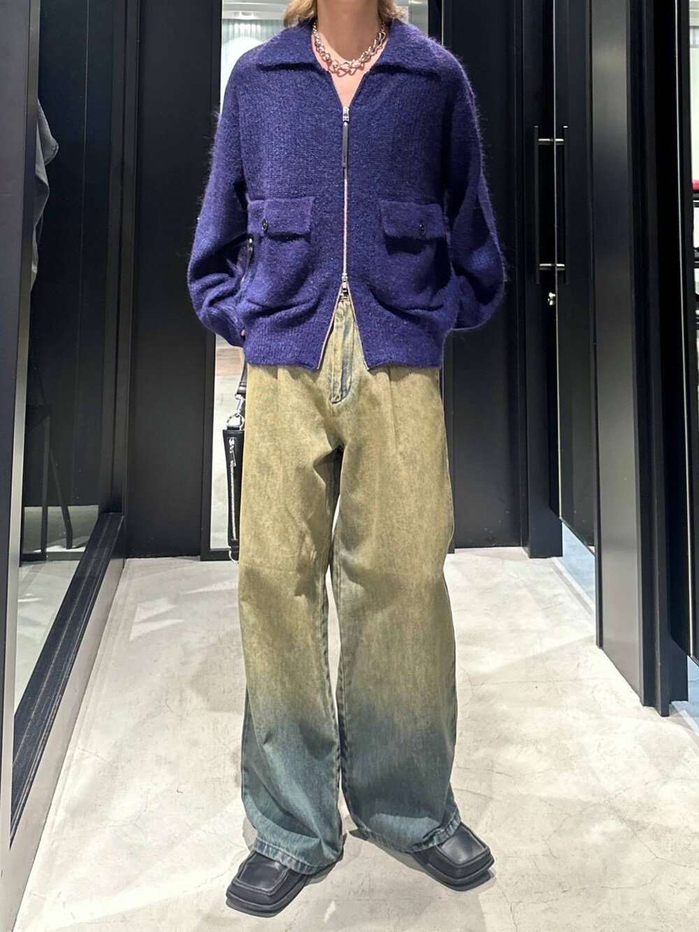 グリーン系のデニムパンツ、ブラック系のショルダーバッグ、ブルー系のニット/セーターを着用したメンズの秋コーディネートの2枚目の写真