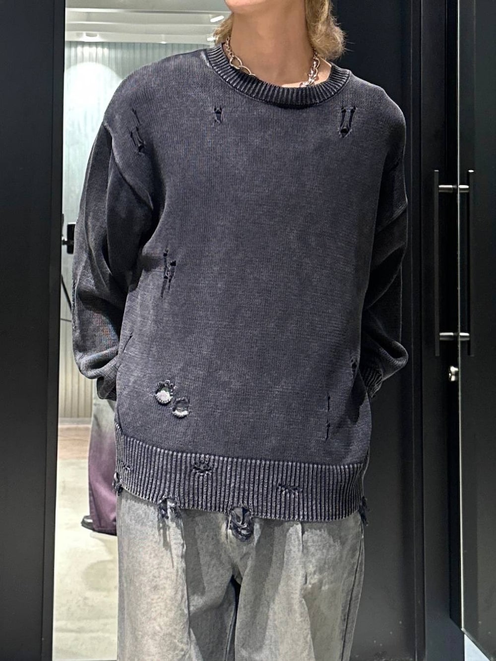 パープル系のデニムパンツ、ブラック系のニット/セーター、シルバー系のネックレスを着用したメンズの秋コーディネートの2枚目の写真