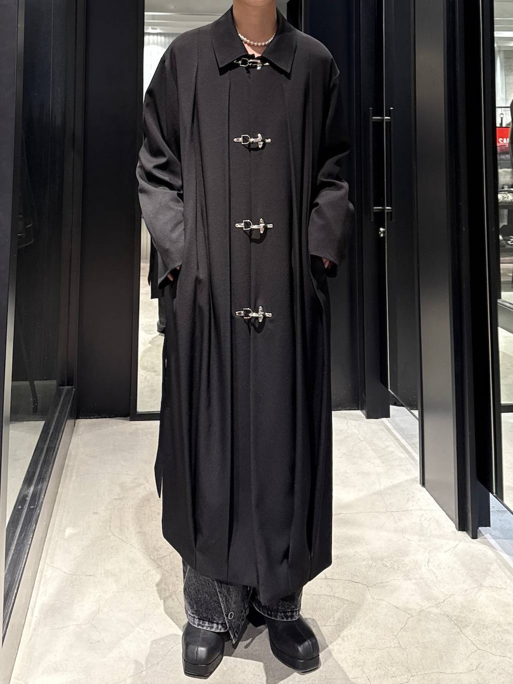 ブラック系のブーツ、ブラック系のステンカラーコート、ブラック系のデニムパンツを着用したメンズの冬コーディネートの3枚目の写真