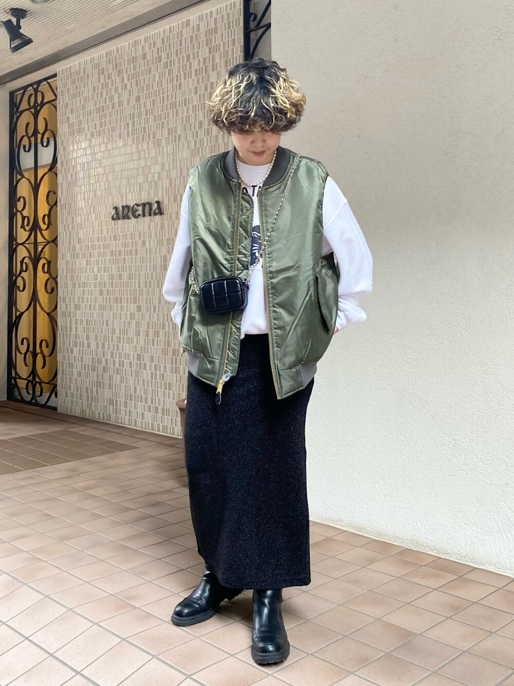 グリーン系のベスト、ブラック系のスカート、ホワイト系のスウェットを着用したレディースの冬コーディネートの2枚目の写真