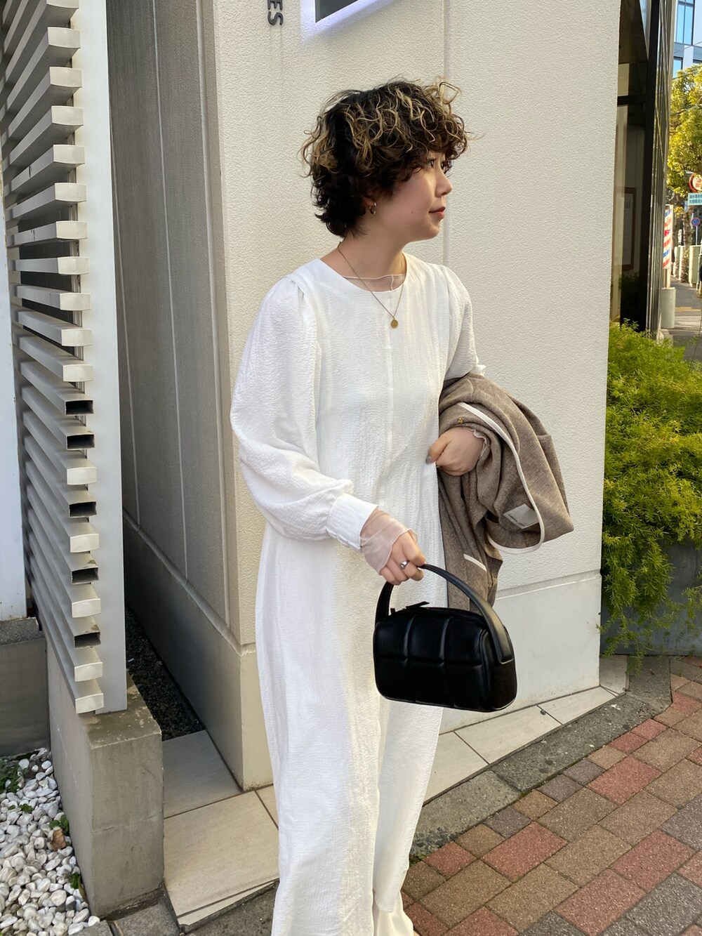 ベージュ系のノーカラーコート、ホワイト系のワンピース、ブラック系のハンドバッグを着用したレディースの冬コーディネートの2枚目の写真